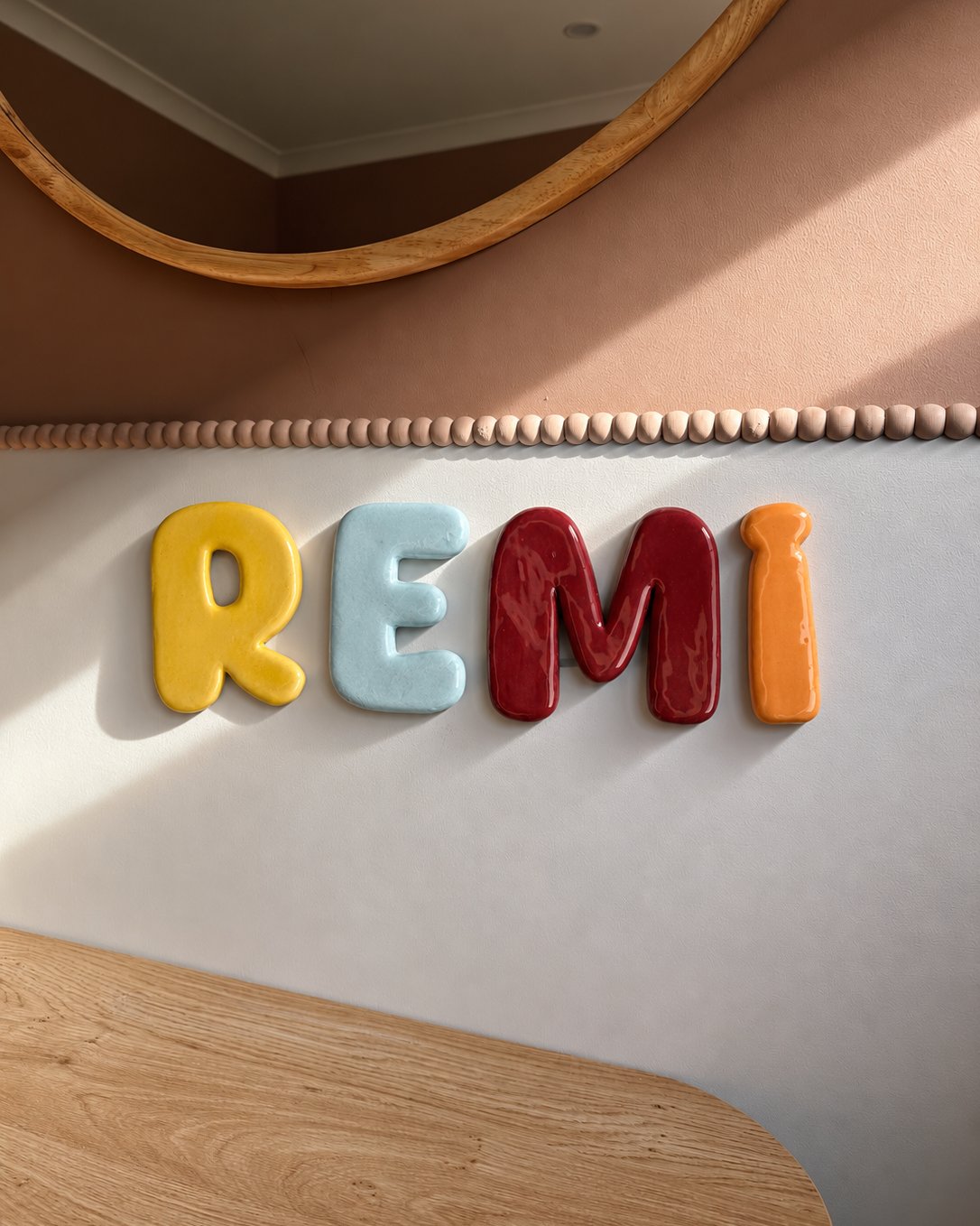 Prénom REMI en lettres de céramique émaillée jaune, bleu ciel, rouge et orange au mur d'une chambre d'enfant