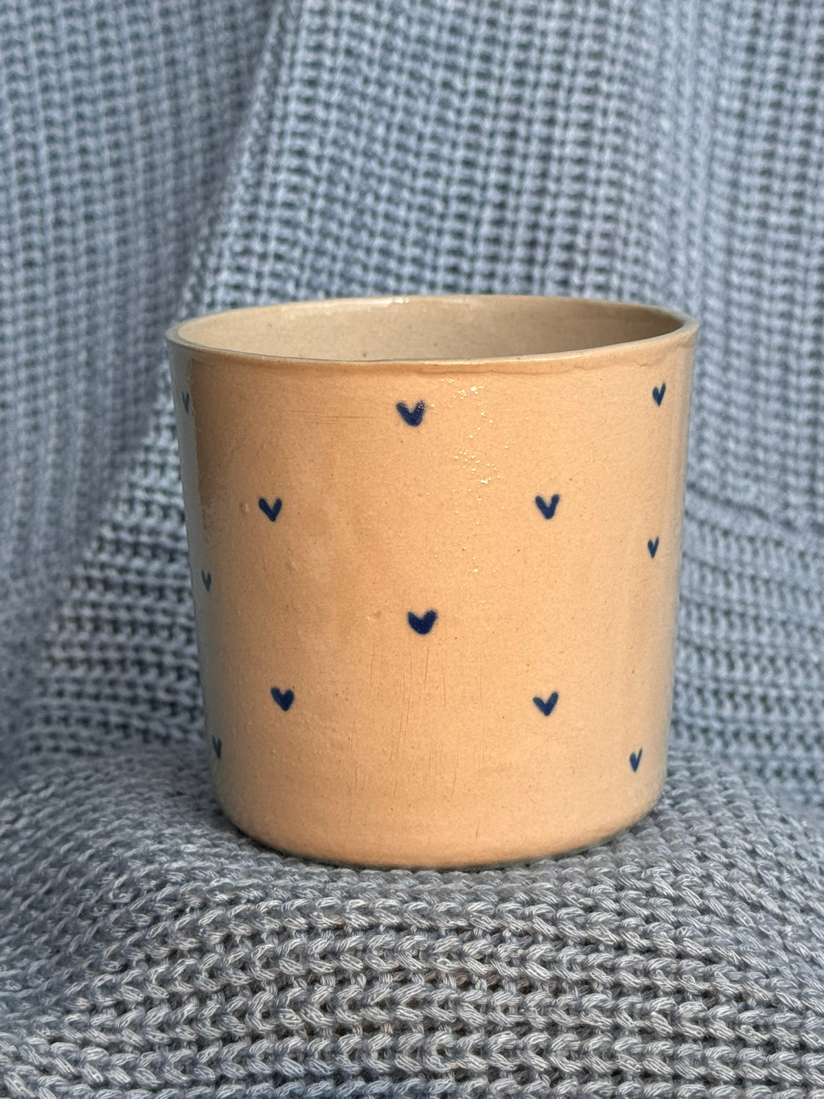 Tasse en céramique beige à petits cœurs bleus, posée sur un plaid