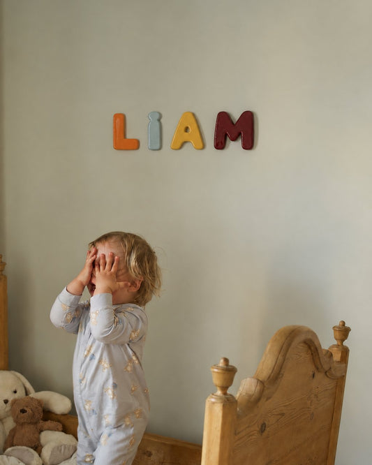 Prénom LIAM en lettres de céramique colorées au mur d'une chambre de bébé, au-dessus du lit